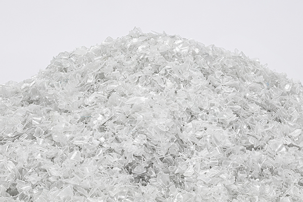 Plastic flakes formed by shredding recycled plastic bottles, part of the process of mechanical recycling of plastics.